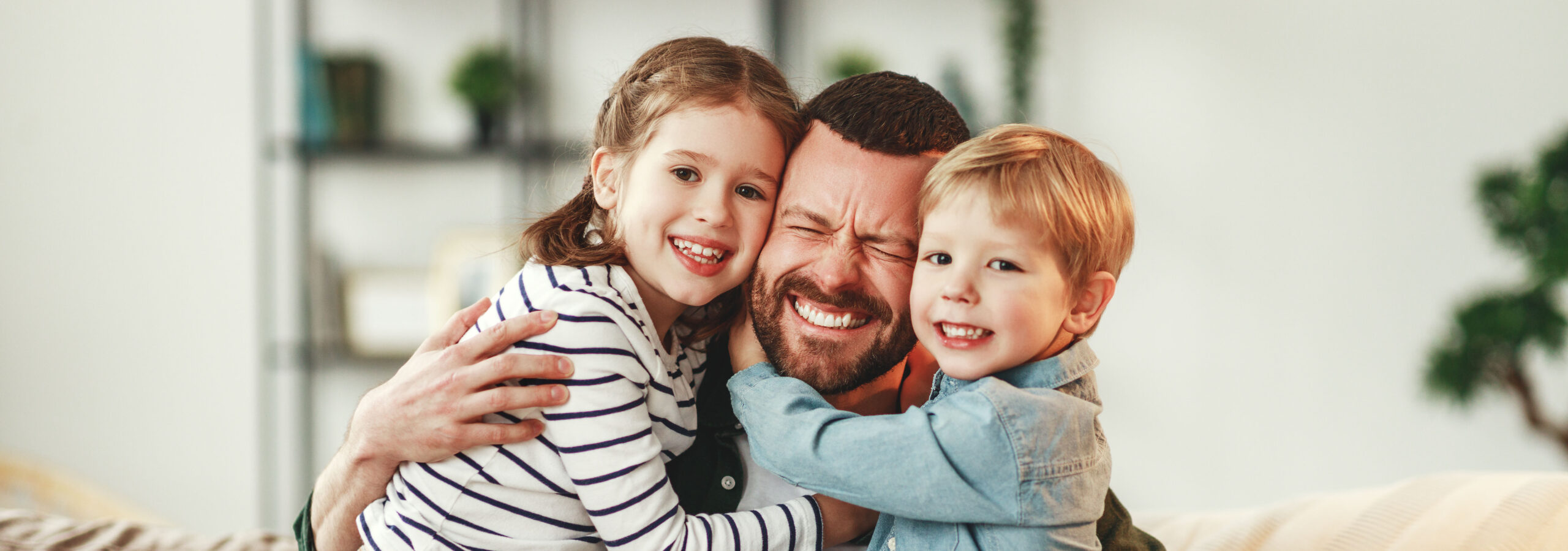 Little siblings congratulating happy father at home Adorable smiling little sister and brother hugging happy dad with gift box in hand while giving congratulations on fathers day at home